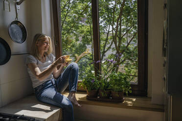 Frau sitzt mit Kaffeetasse in der Nähe des Fensters zu Hause - RIBF01246