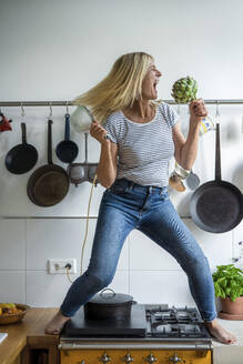 Carefree woman having fun enjoying with artichoke in kitchen - RIBF01254