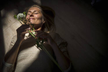 Mature woman lying down with flowers on floor at home - RIBF01267