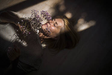 Mature woman with eyes closed holding flowers at home - RIBF01268