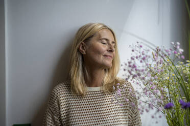 Smiling mature woman with eyes closed in front of wall - RIBF01270