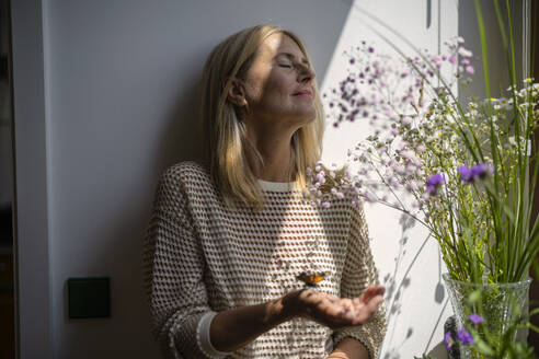 Mature woman standing with butterfly on hand at home - RIBF01275