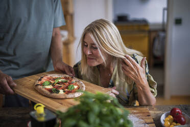 Reife Frau mit blonden Haaren schaut sich eine Pizza an - RIBF01283