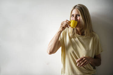 Reife Frau trinkt Kaffee vor einer Wand - RIBF01305