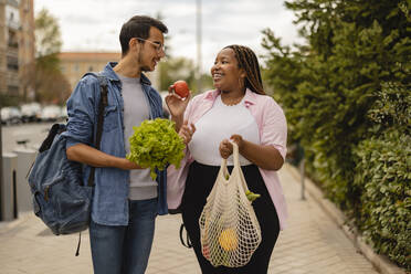 Glückliche Frau zeigt ihrem Freund auf dem Fußweg stehend Gemüse - JCCMF08047