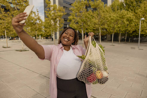 Glückliche Frau mit Tasche von Gemüse, die selfie durch smart phone nimmt - JCCMF08055