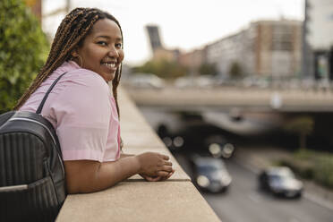 Happy young woman with backpack leaning on wall - JCCMF08116