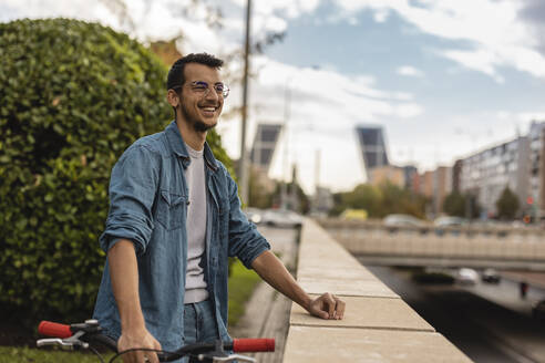 Glücklicher junger Mann mit Fahrrad an der Wand stehend - JCCMF08118