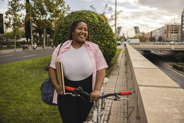 Glückliche junge Frau mit Fahrrad auf dem Gehweg stehend - JCCMF08139