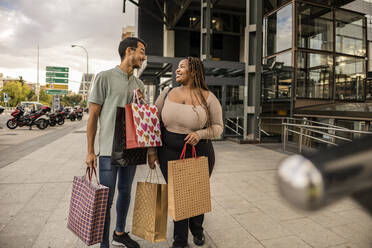 Glückliches junges Paar mit Einkaufstüten auf dem Fußweg stehend - JCCMF08141