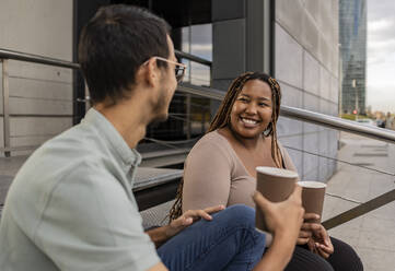 Smiling young couple with coffee cups sitting on steps - JCCMF08144