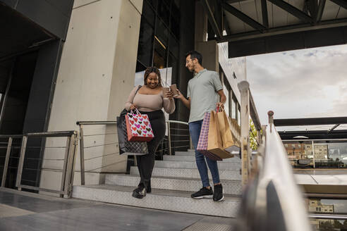 Glückliches junges Paar geht mit Einkaufstaschen und stößt mit Kaffeetassen auf einer Treppe an - JCCMF08145