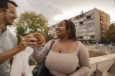 Smiling young couple with snacks standing in front of building - JCCMF08147