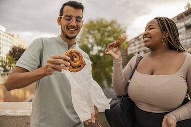 Happy man and woman with sweet food standing under sky - JCCMF08148