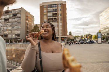 Happy young woman eating sweet food with man at footpath - JCCMF08151