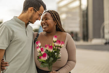 Happy young man embracing woman standing with bouquet of flowers - JCCMF08159