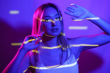 Young woman with neon colored lighting in front of wall - JSMF02496