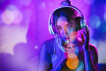 Young woman with headphones listening to music in front of wall - JSMF02500