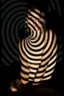 Young woman with illuminated spiral pattern against black background - JSMF02507