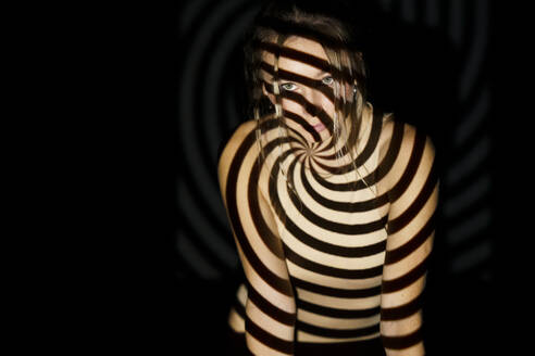 Frau mit spiralförmigem beleuchtetem Muster auf dem Körper vor schwarzem Hintergrund - JSMF02508