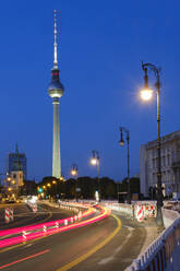 Germany, Berlin, Vehicle light trails stretching along illuminated street at night with Berlin Television Tower in background - WIF04636