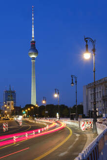 Germany, Berlin, Vehicle light trails stretching along illuminated street at night with Berlin Television Tower in background - WIF04636