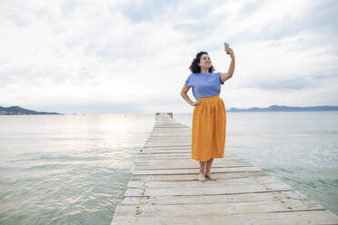 Frau nimmt Selfie durch Smartphone stehend auf Steg - JOSEF14781