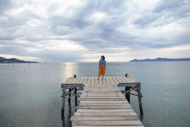 Frau steht auf einem Steg inmitten des Meeres unter bewölktem Himmel - JOSEF14782
