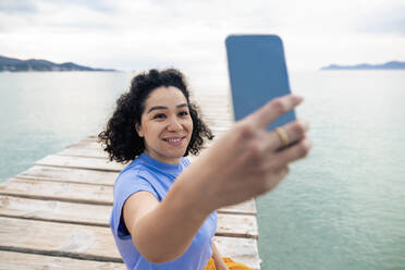 Woman taking selfie sitting on jetty at sea - JOSEF14799