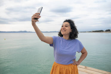 Lächelnde Frau nimmt Selfie vor dem Meer - JOSEF14809