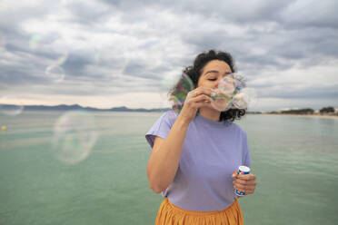 Frau hat Spaß beim Blasen von Seifenblasen vor dem Meer - JOSEF14813
