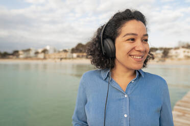 Happy woman listening to music wearing headphones by sea - JOSEF14820