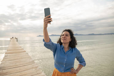 Woman searching mobile phone network on jetty - JOSEF14836