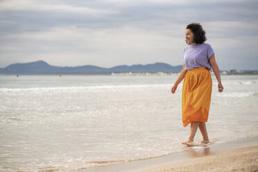 Lächelnde Frau, die bei Sonnenuntergang am Strand spazieren geht - JOSEF14841