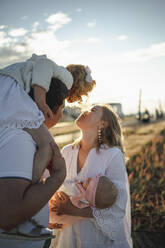 Happy mother and father enjoying with daughters on sunny day - ANAF00552