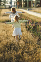 Happy girls with arms outstretched walking on grass - ANAF00556