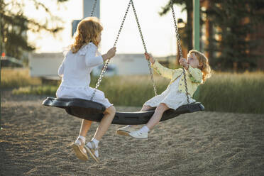 Happy girls swinging on swing at park - ANAF00566