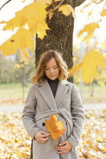 Schwangere Frau mit Ahornblatt an einem Baum lehnend im Herbstpark - ONAF00267