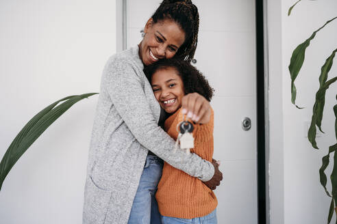 Happy mature woman hugging daughter showing house keys - EBBF07214