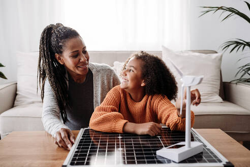 Happy mother and daughter sitting with renewable energies at home - EBBF07220