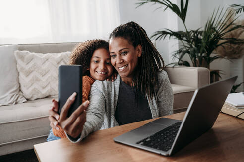 Happy mother and daughter talking on video call through smart phone at home - EBBF07227