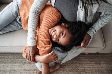 Happy girl lying on mother's lap in living room at home - EBBF07231