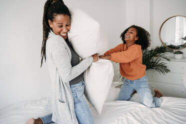 Fröhliche Mutter und Tochter spielen mit Kissen auf dem Bett zu Hause - EBBF07247