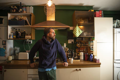 Mann steht in beleuchteter Küche zu Hause - PMF02265