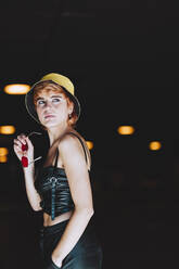 Thoughtful young woman holding sunglasses at underpass - IFRF01889