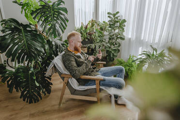 Mann mit Smartphone auf einem Stuhl sitzend zu Hause - YTF00335