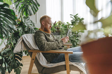 Man using mobile phone sitting on chair at home - YTF00337