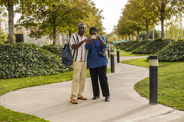 Mann und Frau mit Smartphone auf dem Fußweg im Park - JCCMF08169