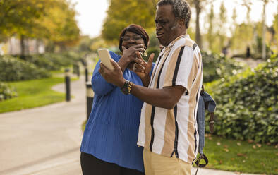 Ältere Frau lacht über Mann mit Smartphone im Park - JCCMF08183