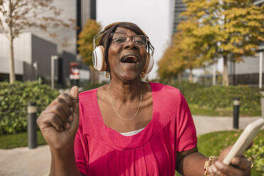 Happy woman wearing wireless headphones enjoying at park - JCCMF08201